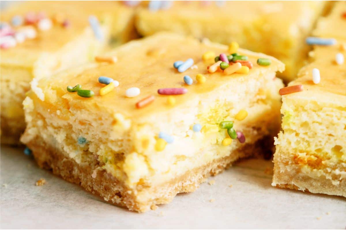 Side view of one cheesecake bar cut into squares lined up with other cheesecake bars.