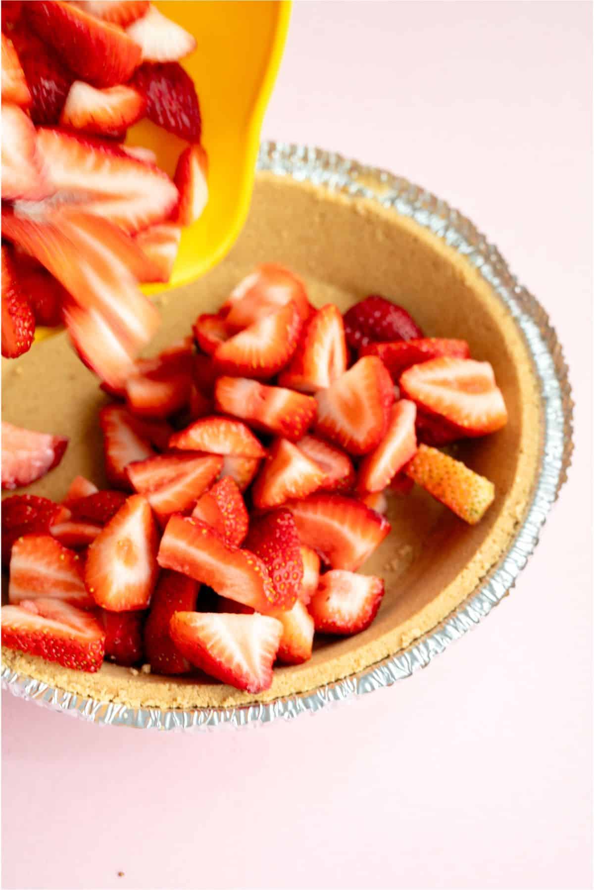 Dumping fresh sliced strawberries into pie crust