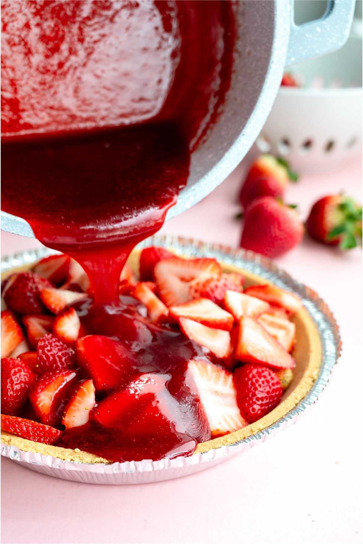 Pouring strawberry sauce on top of strawberries in pie crust