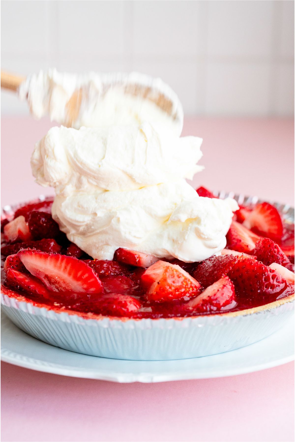 Spreading whipped topping on top of cold Fresh Strawberry PIe