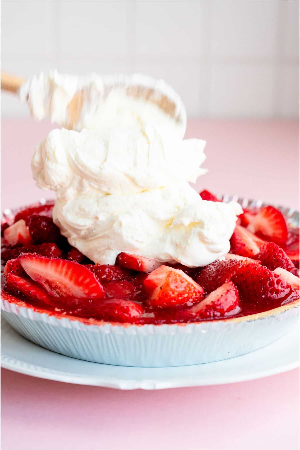 Wooden spoon spooning whip cream on top of pie.