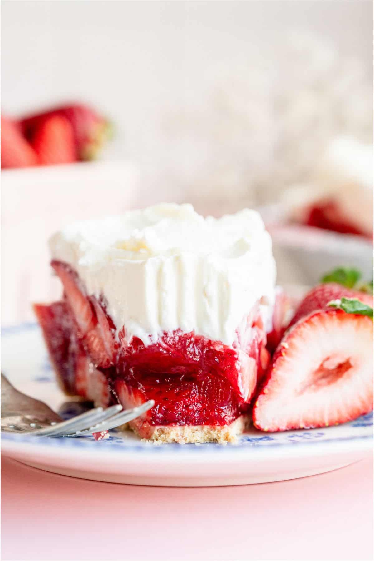 A slice of fresh strawberry pie on a plate with a fork taking a slice of it.