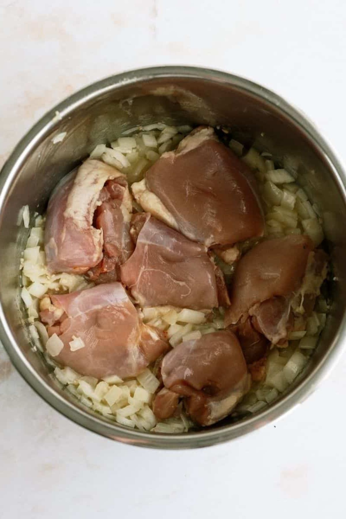 Chicken thigh pieces mixed with chopped onion and butter in the Instant Pot.