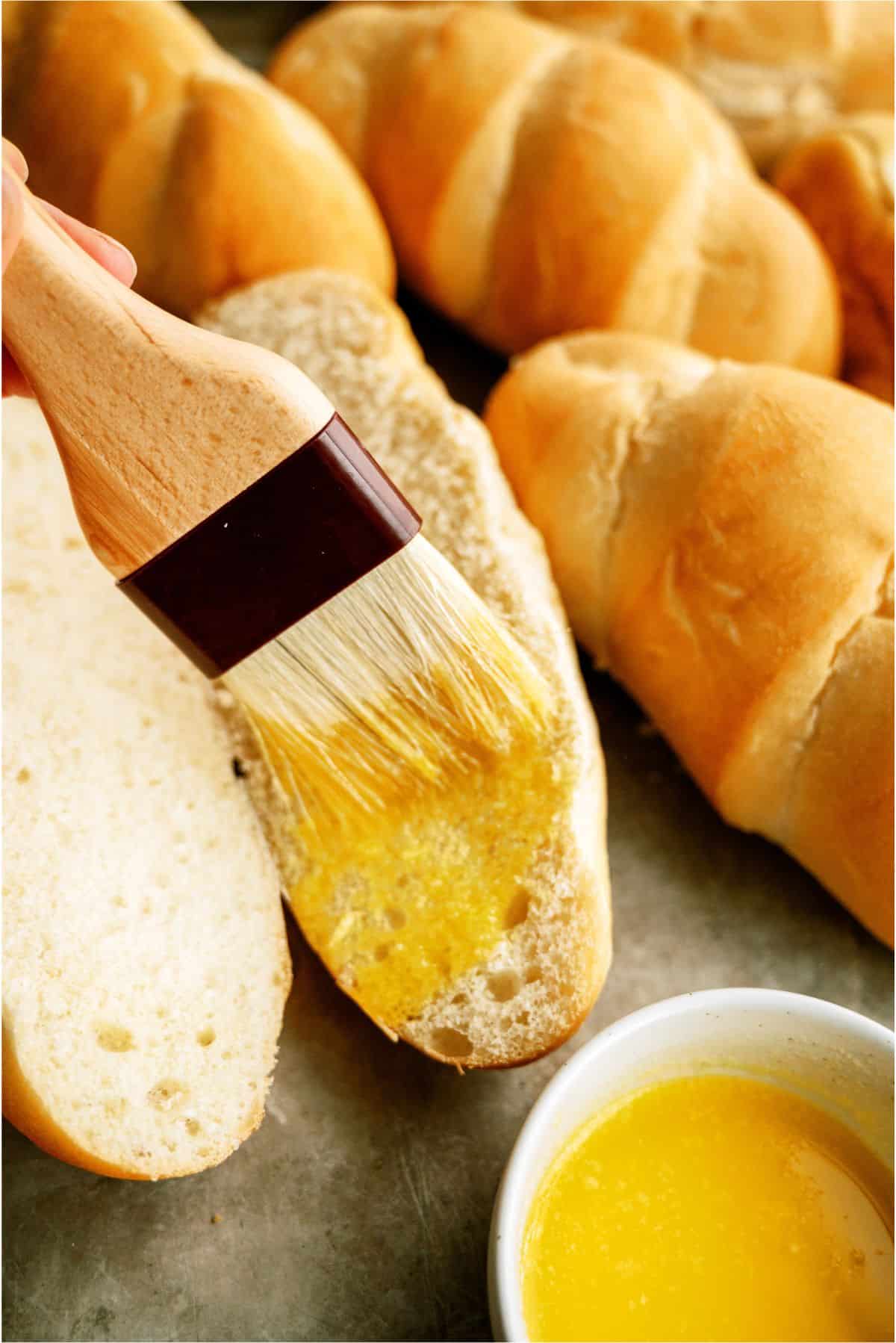 Brushing melted butter on hoagie rolls