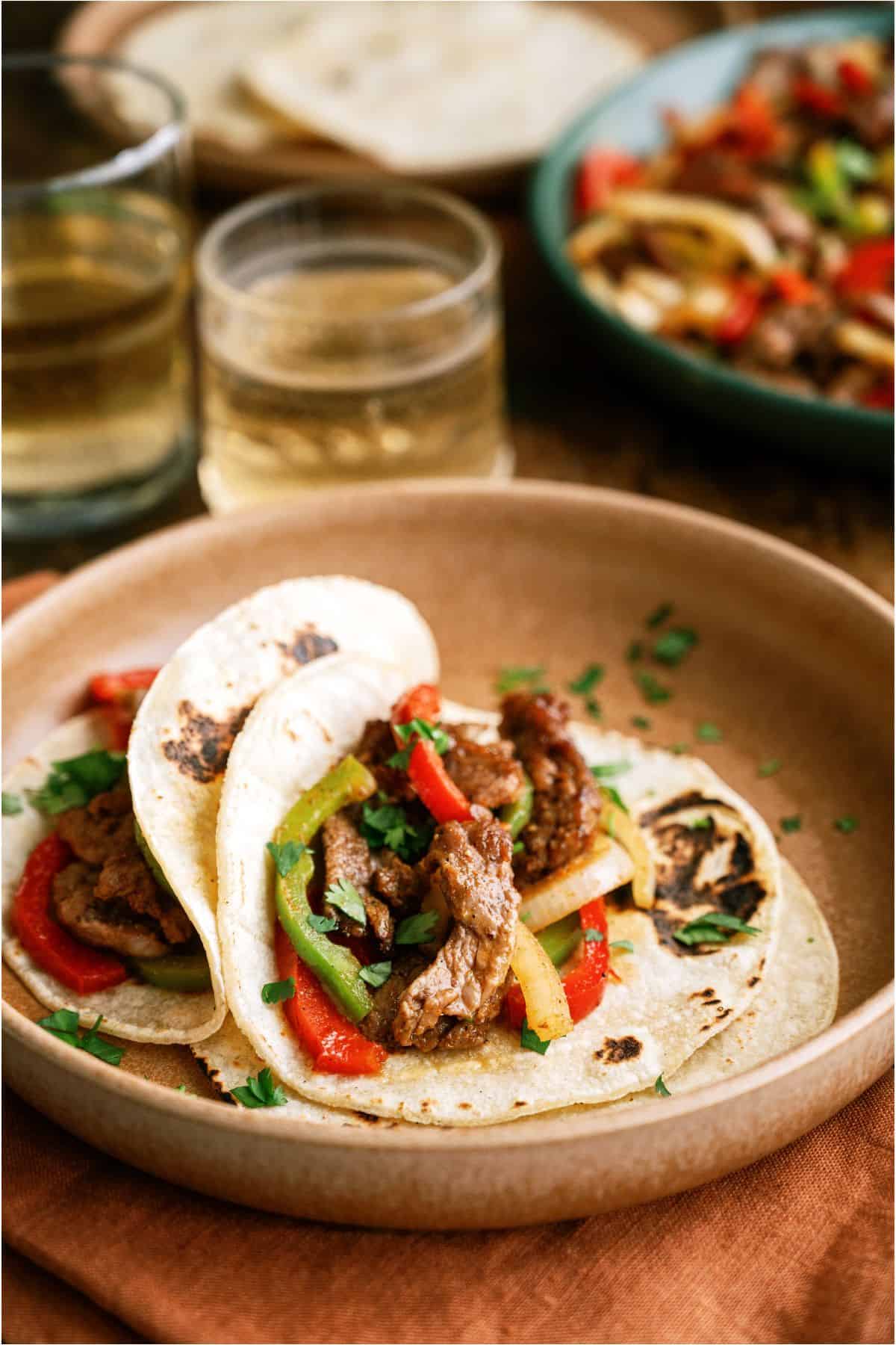 Two Sheet Pan Steak Fajitas on flour tortillas on a plate.