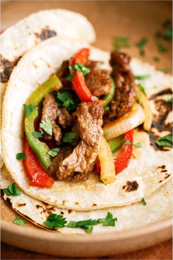 A flour tortilla filled with Sheet Pan Steak Fajitas.