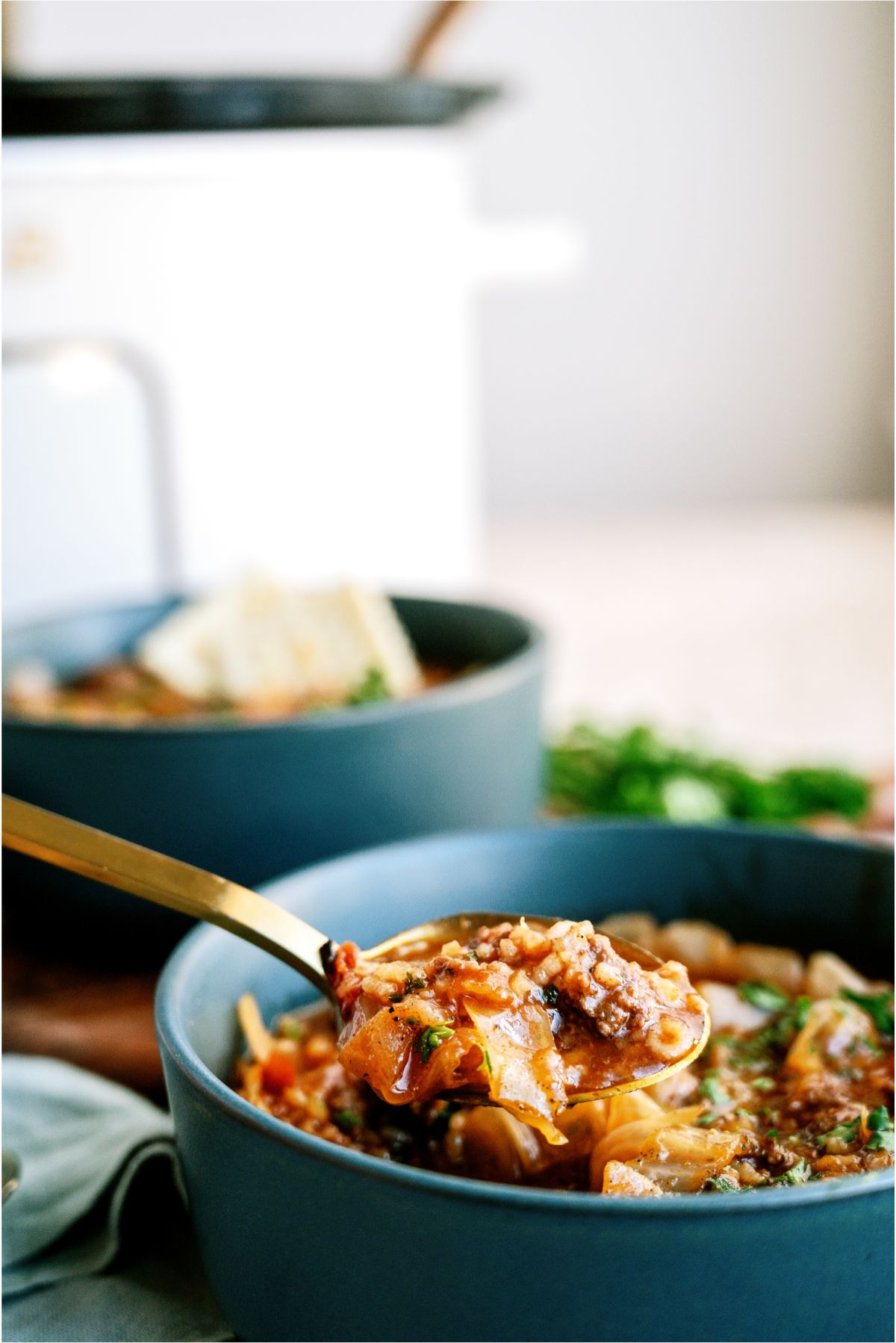 A bowl of Slow Cooker Cabbage Roll Soup with a spoon, and a slow cooker in the background