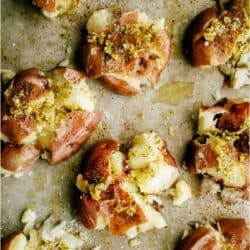 Several smashed red potatoes on a parchment-lined baking sheet, seasoned with herbs and spices, ready for roasting.