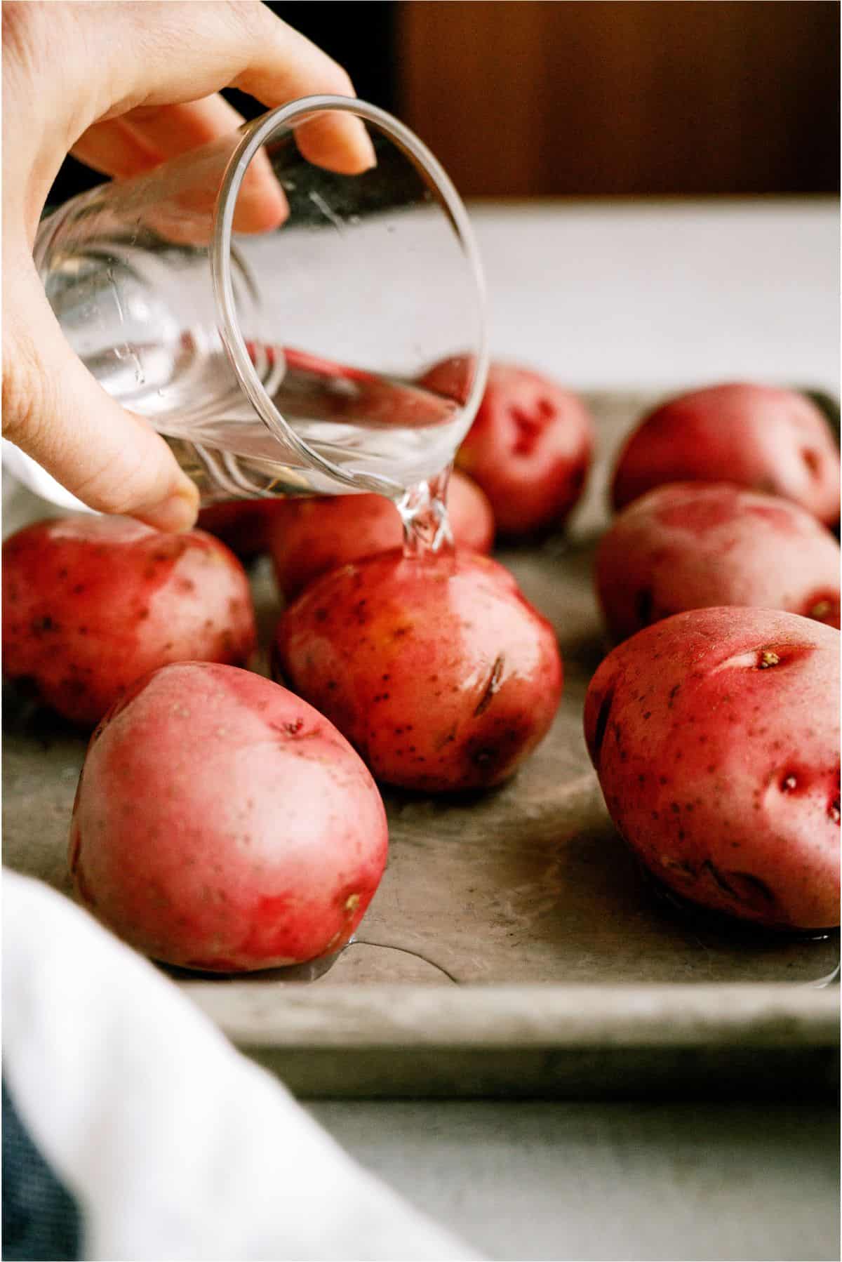 Pouring water onto baking sheet with potatoes