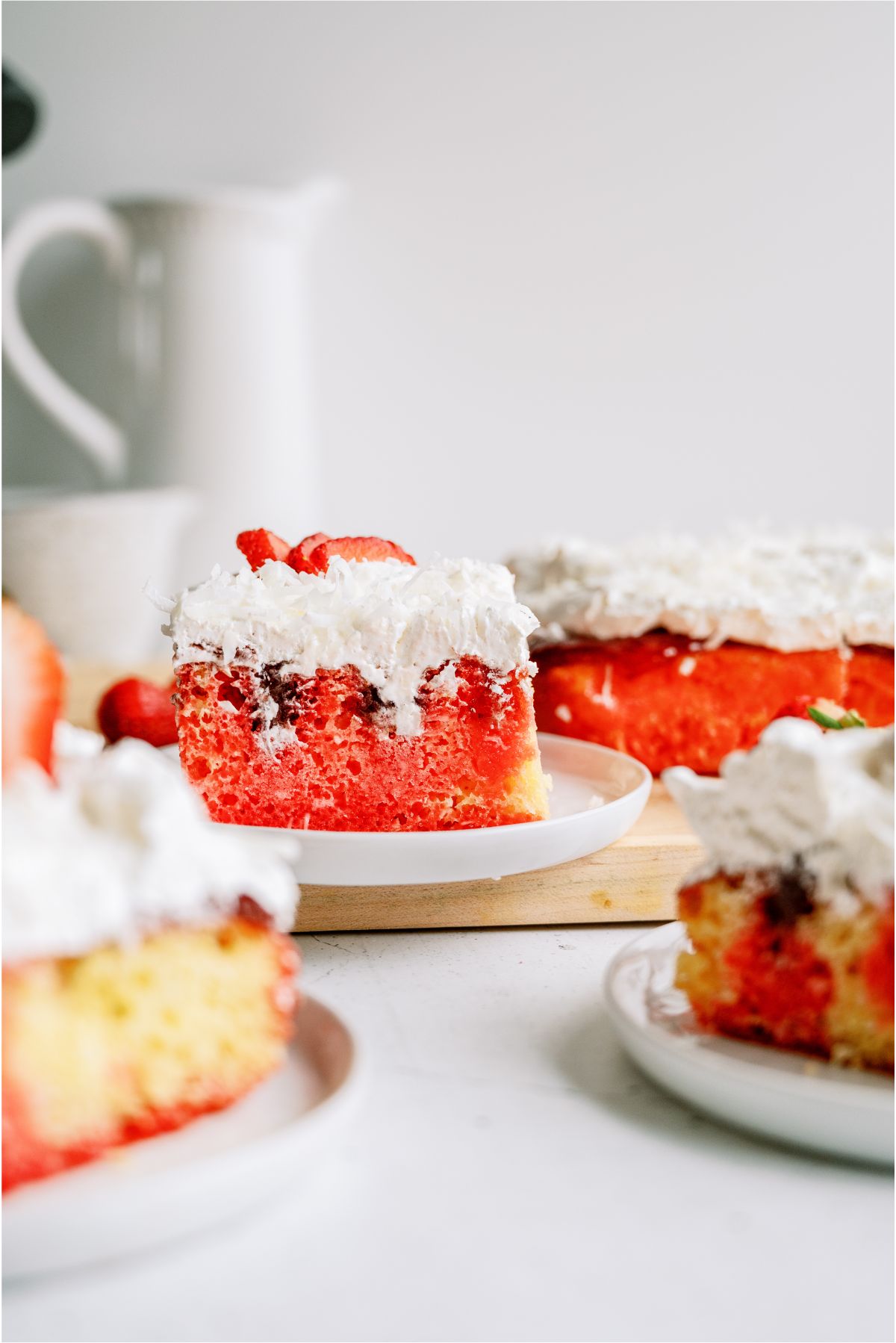 Slices of Strawberry Coconut Poke Cake on plates topped with fresh strawberries