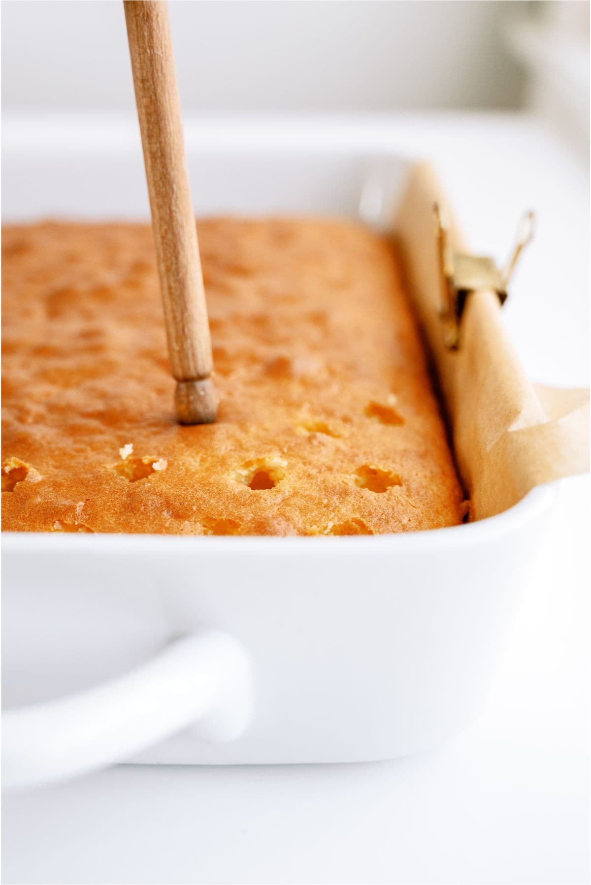 Poking holes in a baked cake with the end of a wooden spoon.