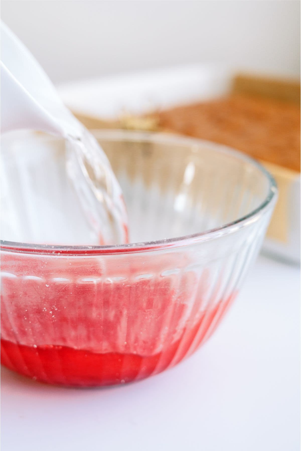 Making strawberry jello mixture in a glass bowl.