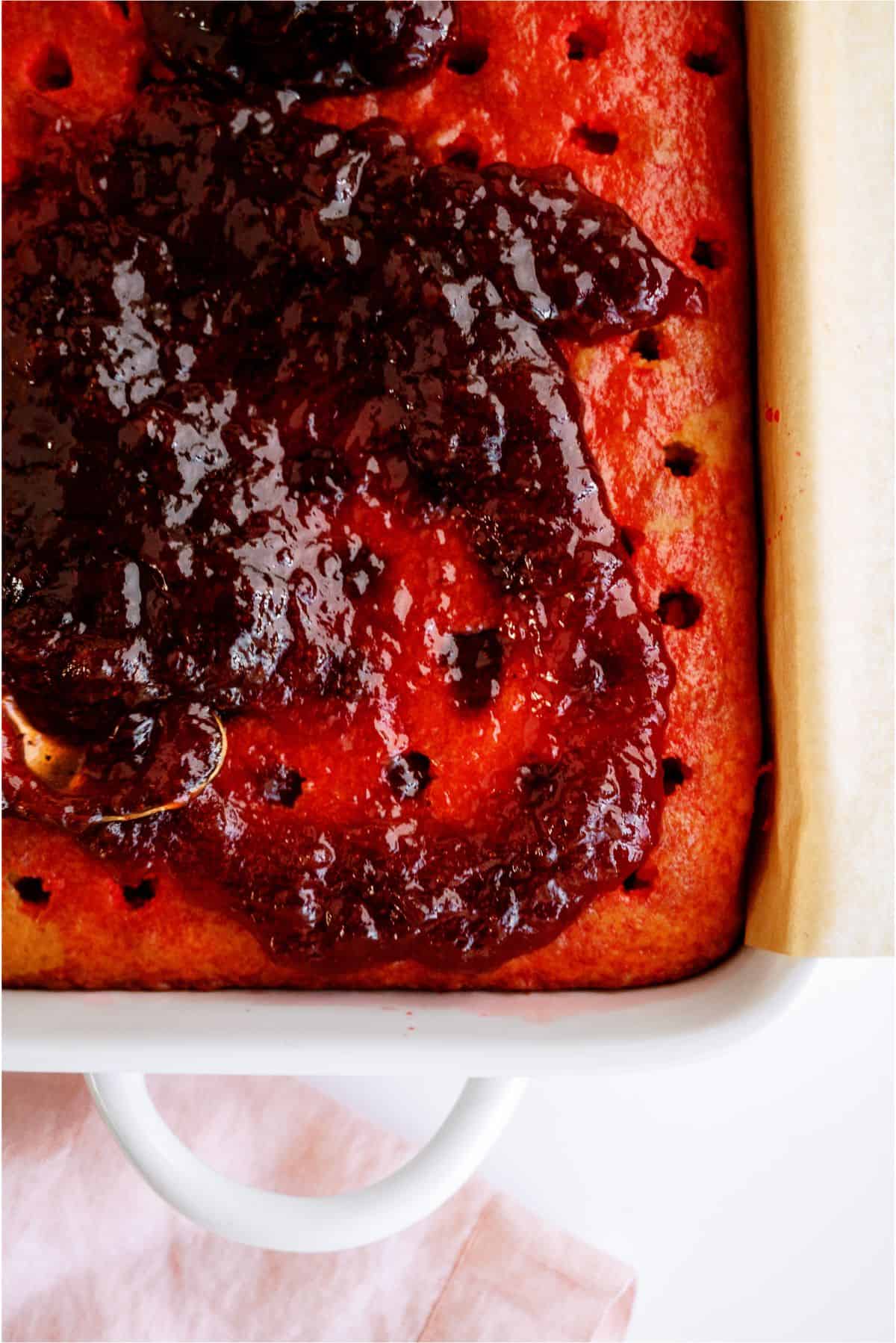 Spreading strawberry preserve on top of poked cake.