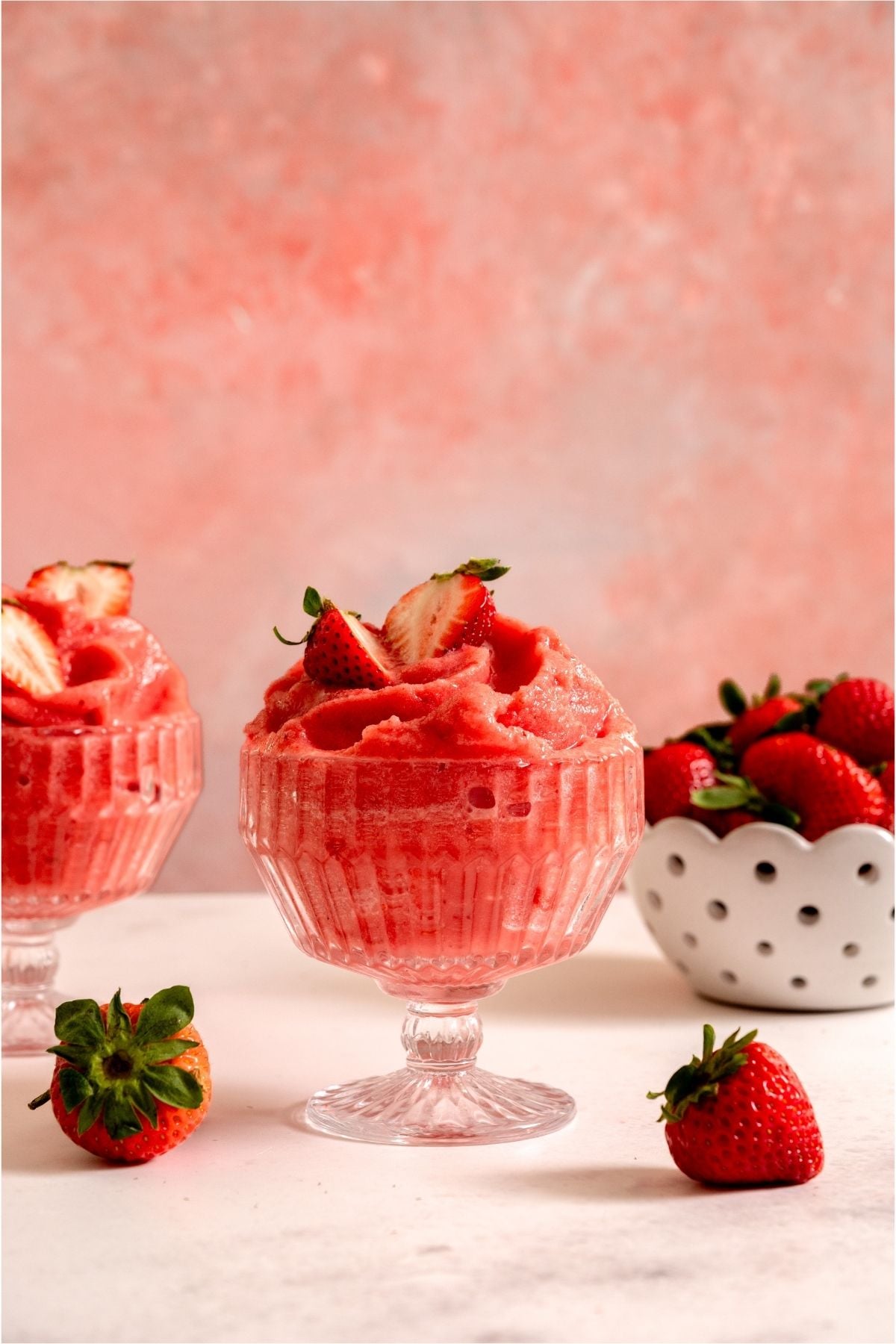 2 glasses of Strawberry Dole Whip with a fresh strawberries in a bowl on the side.