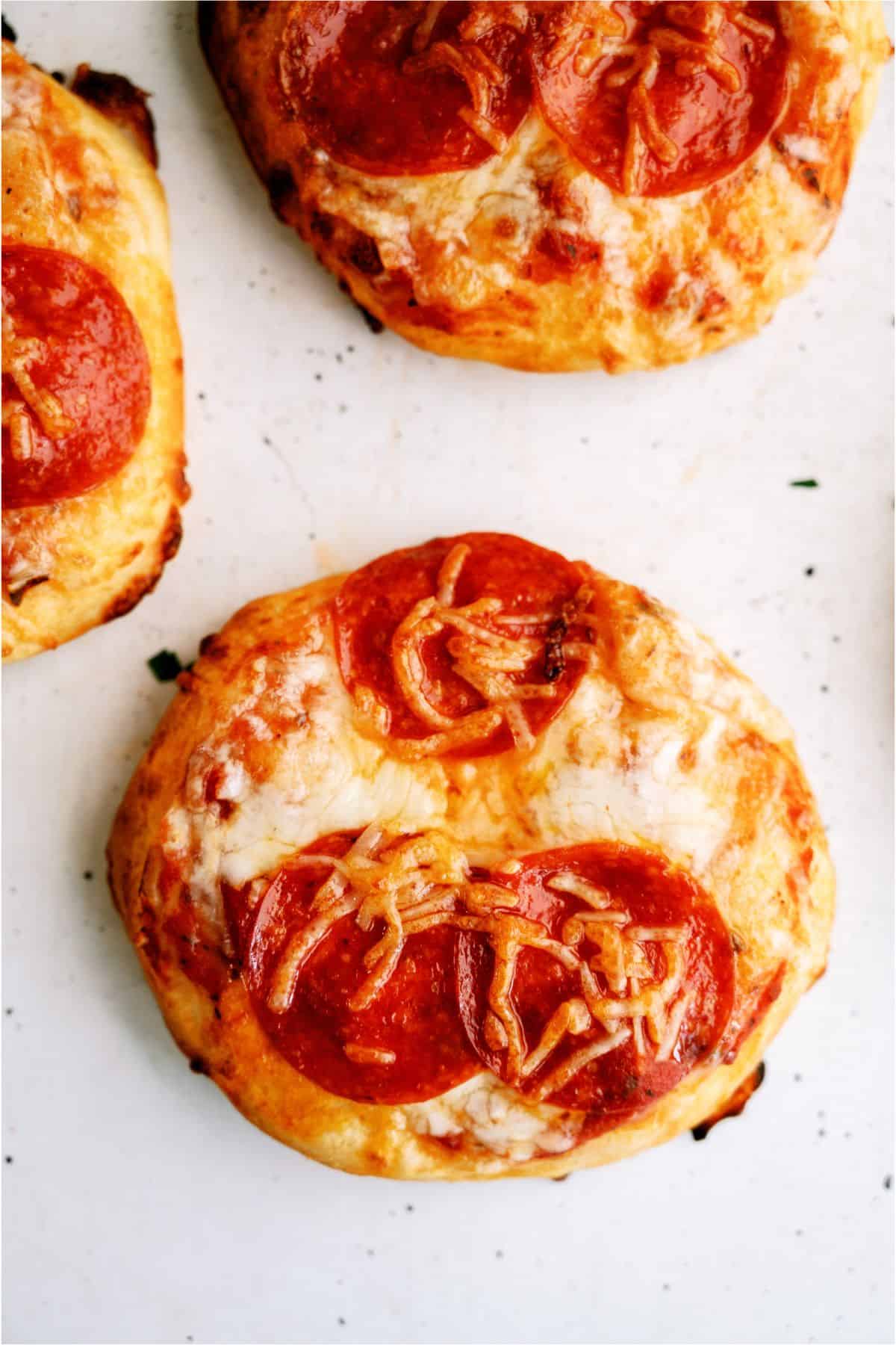 Three mini pepperoni pizzas with melted cheese and pepperoni slices on a white surface.