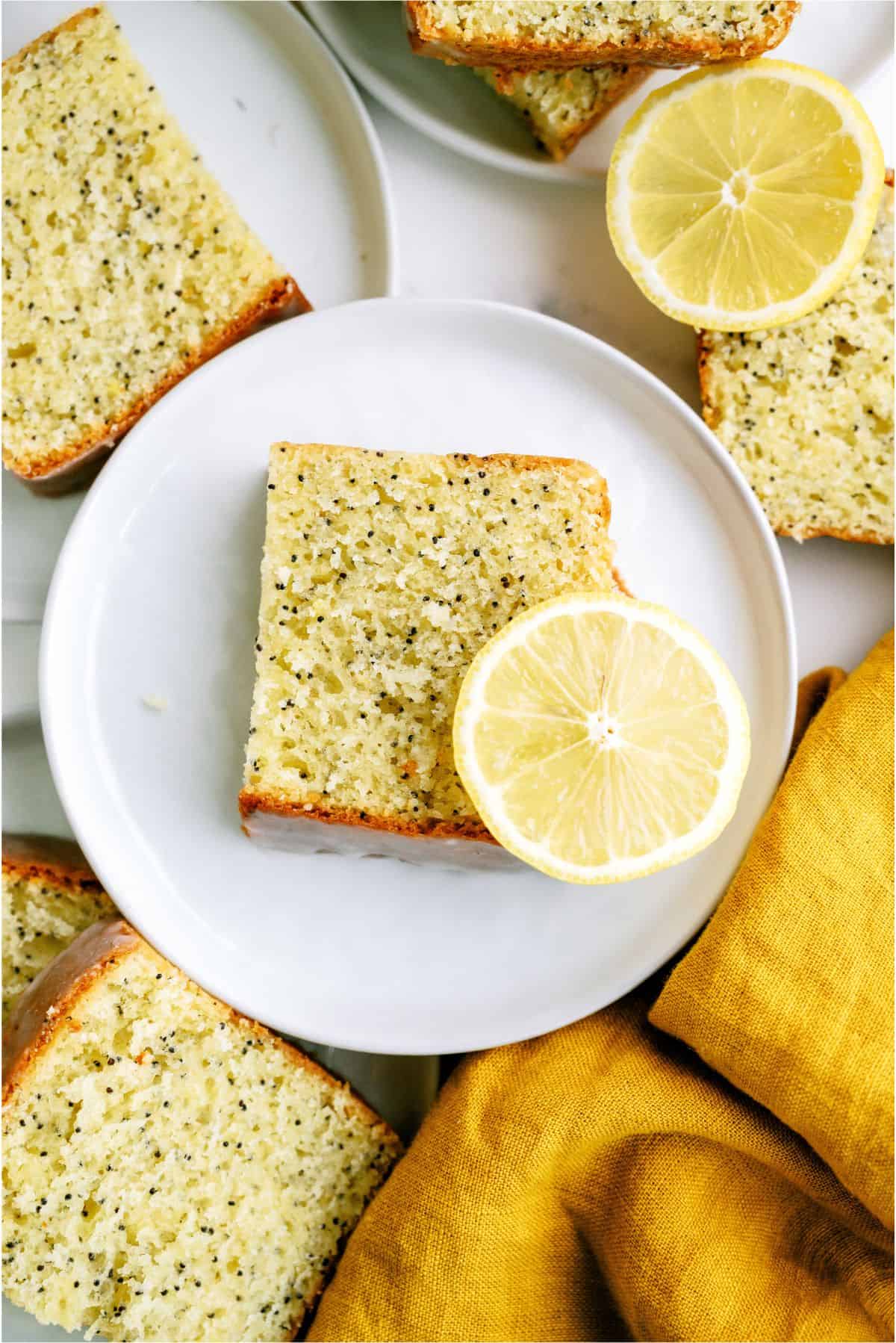 A slice of Glazed Almond Poppy Seed Bread on a plate with a lemon slice