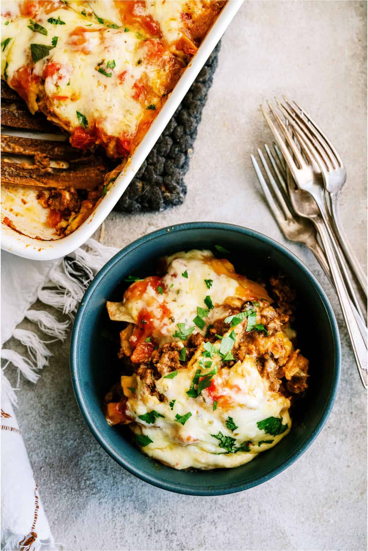 A serving of Ground Beef Firecracker Casserole in a bowl withe the rest of the casserole in the background