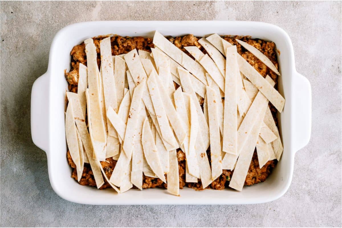 Sliced tortilla strips on top of ground beef mixture in casserole dish