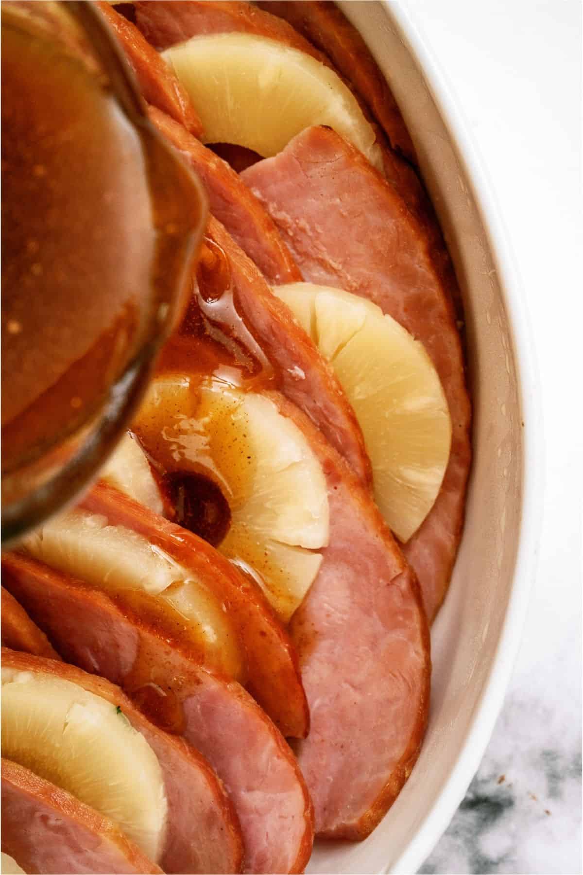 Pouring glaze over Ham and Pineapple Bake in a casserole dish.