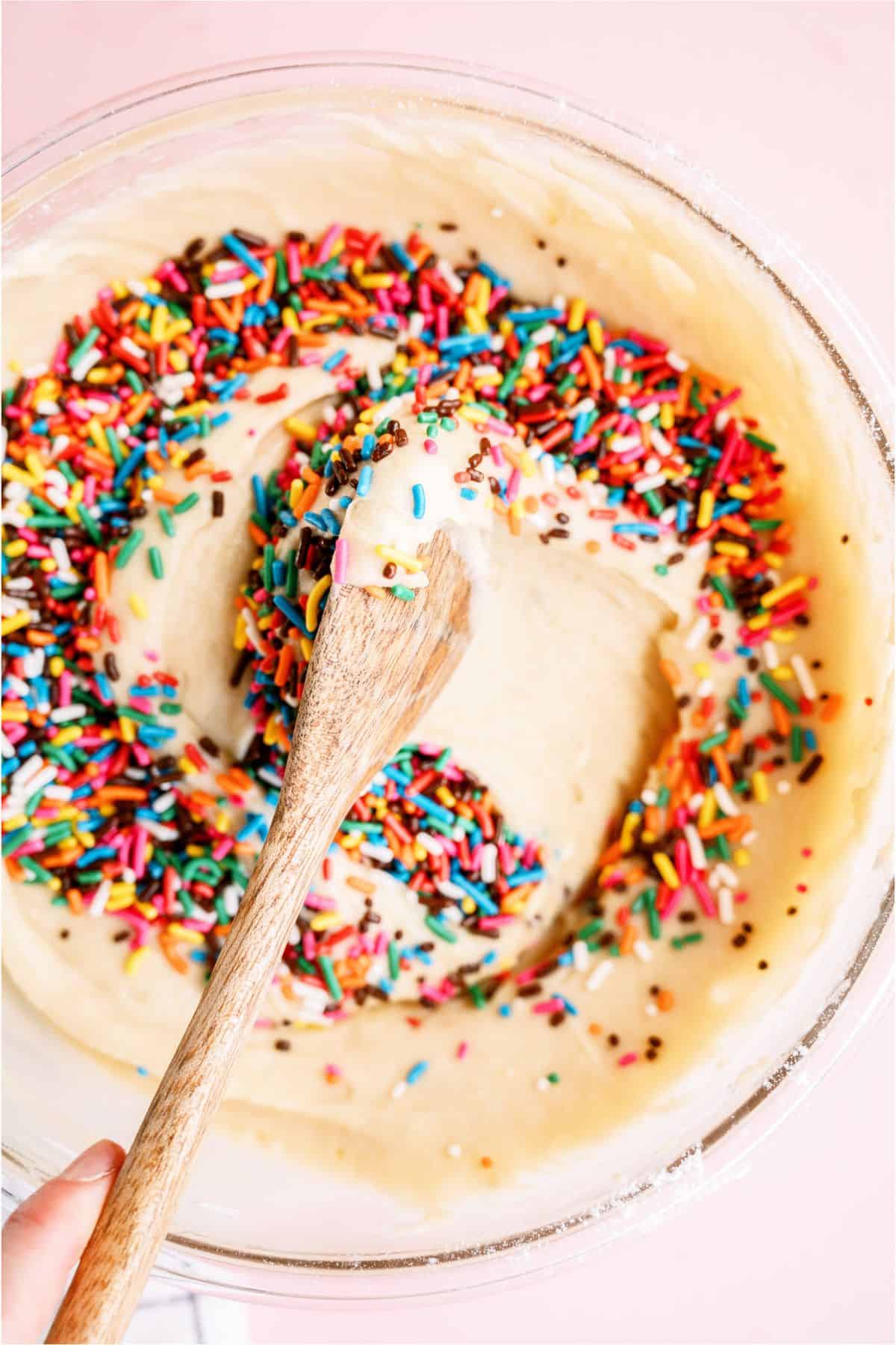 Gently mixing sprinkles into cake batter with wooden spoon