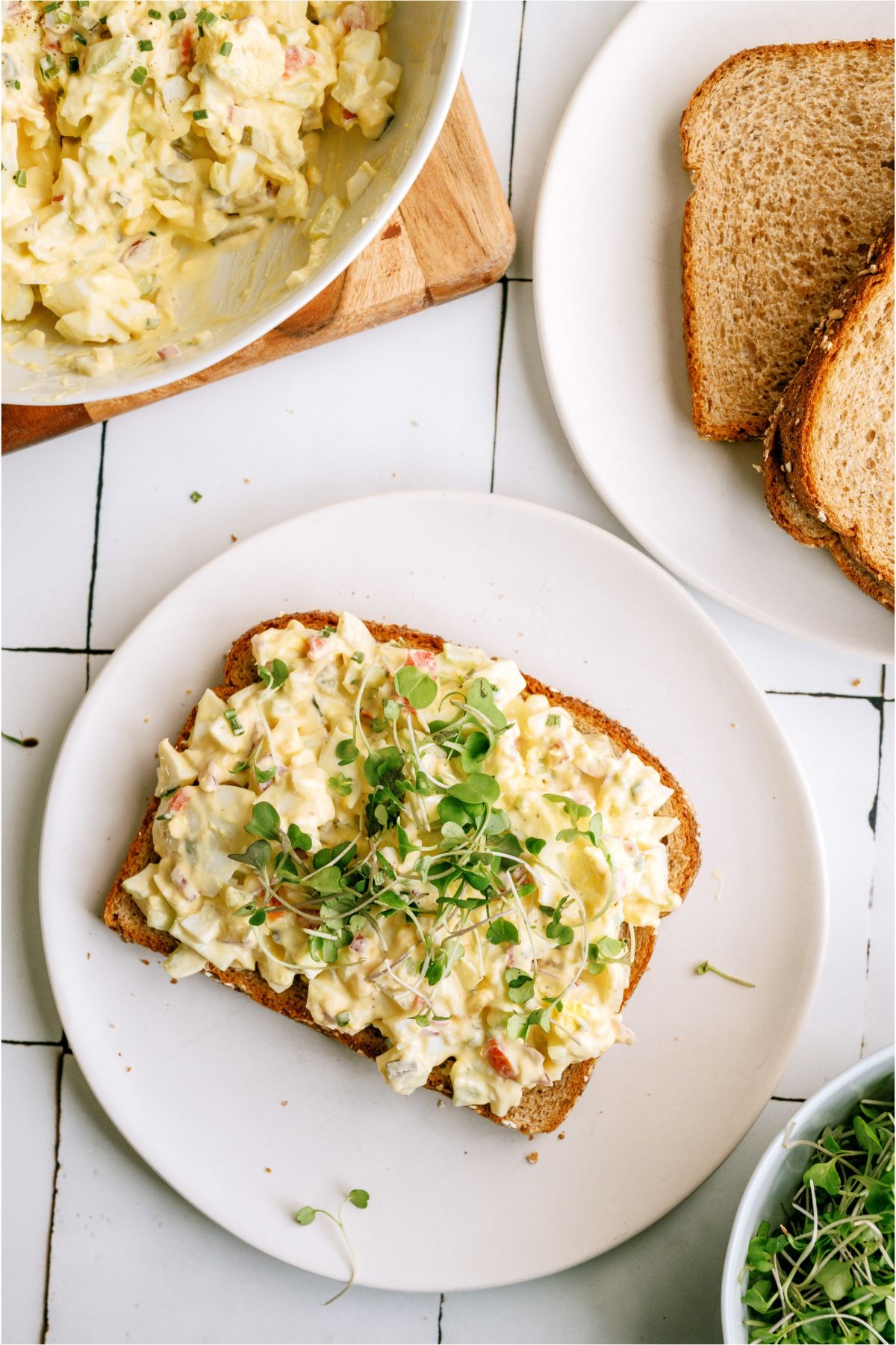 Loaded Egg Salad served on a piece of bread with a bowl of Loaded Egg Salad in the background