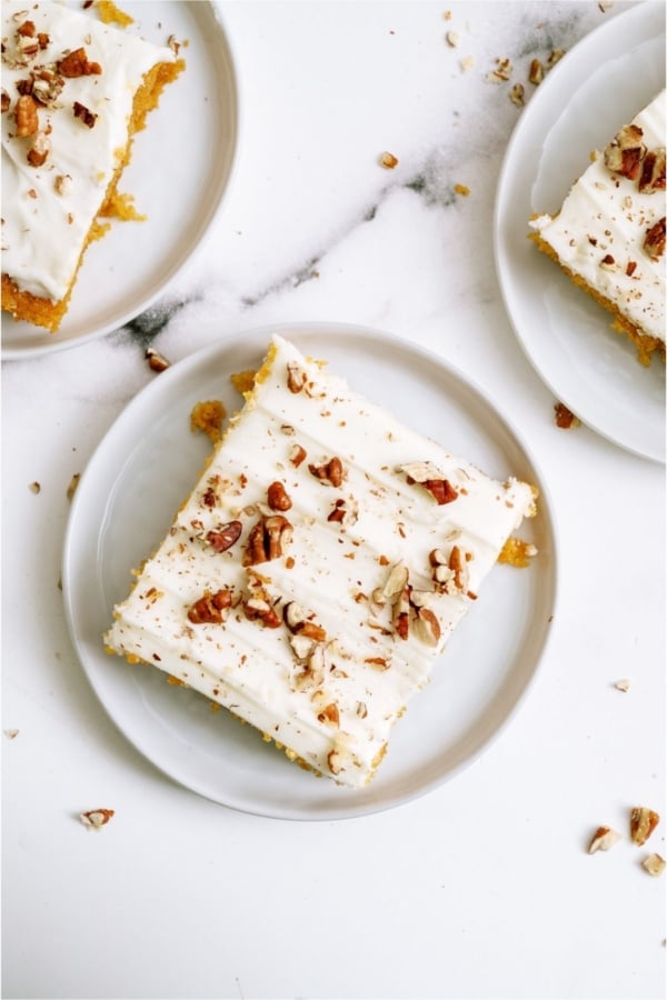Slices of Sheet Pan Carrot Cake and Cream Cheese Frosting on white plates.