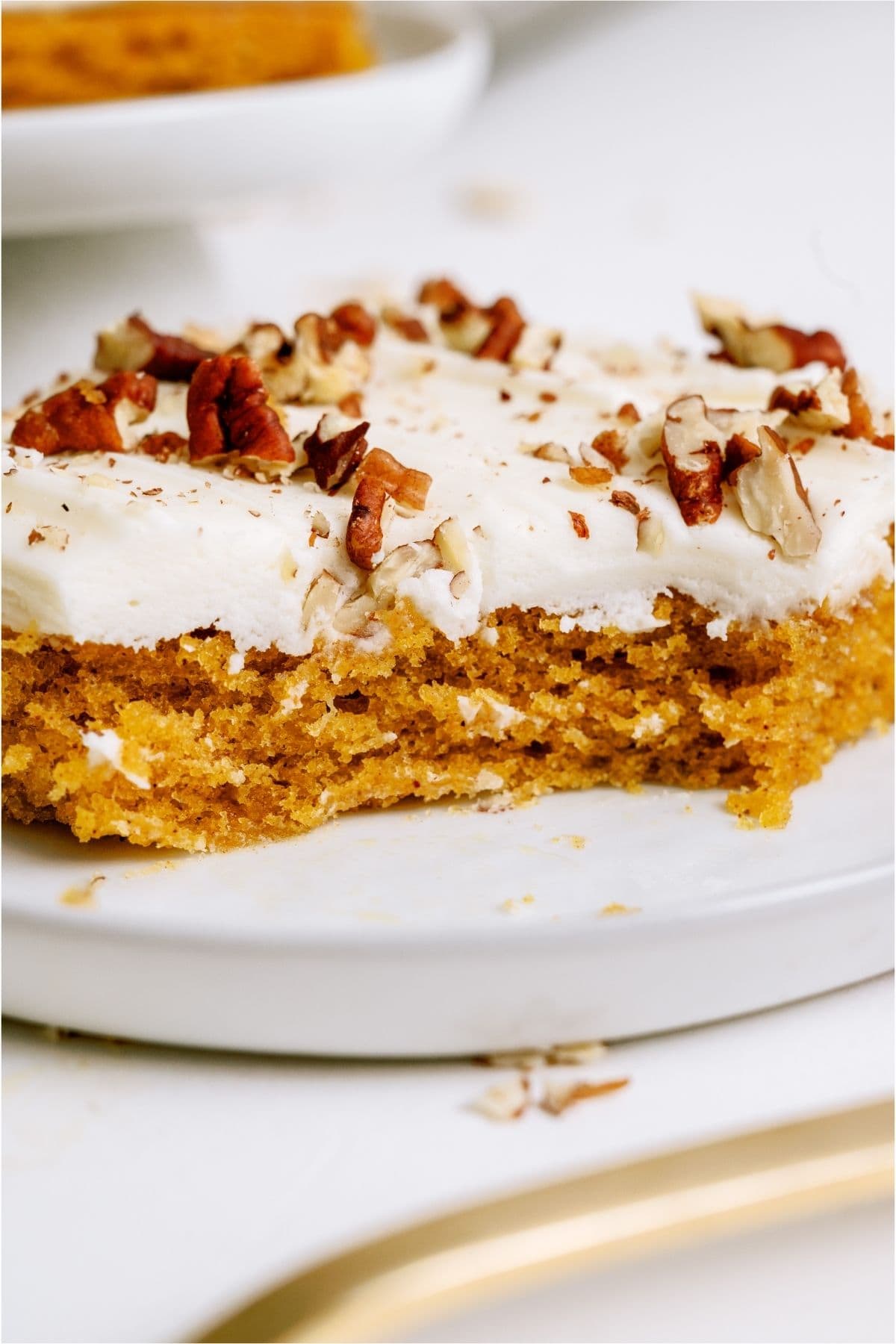 A square of Sheet Pan Carrot Cake and Cream Cheese Frosting on a plate with a bite missing.