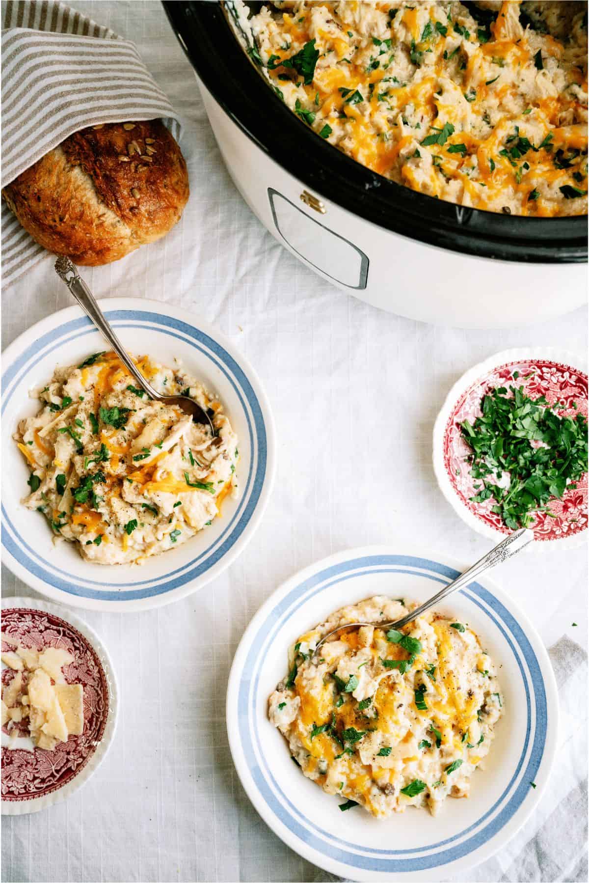 Top view of Slow Cooker Parmesan Chicken And Rice in the slow cooker and 2 servings in bowls