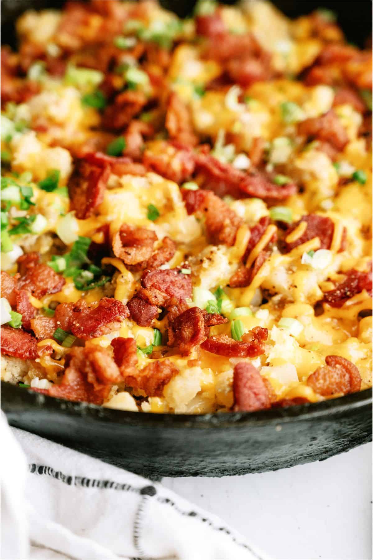 A skillet filled with loaded cheesy potatoes, topped with crispy bacon and chopped green onions.