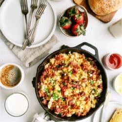 Plate of cheesy scrambled eggs with bacon and green onions, served with a slice of buttered toast. A fork is placed beside the food.