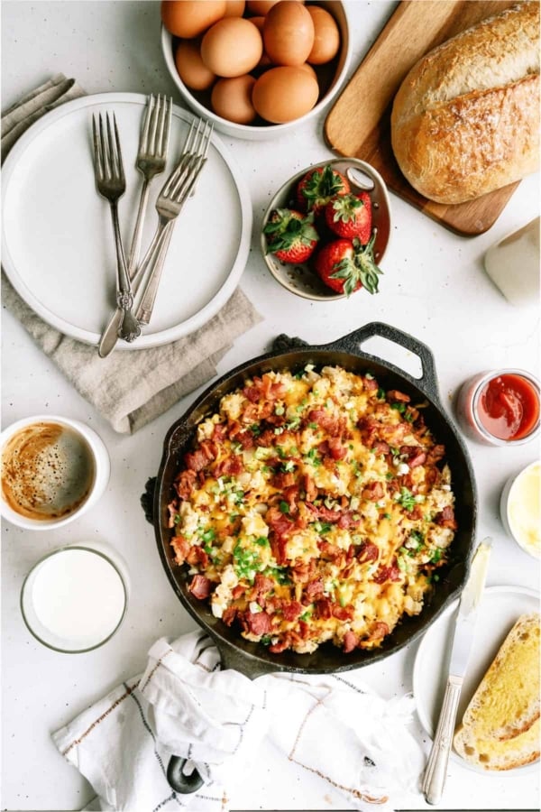 Plate of cheesy scrambled eggs with bacon and green onions, served with a slice of buttered toast. A fork is placed beside the food.