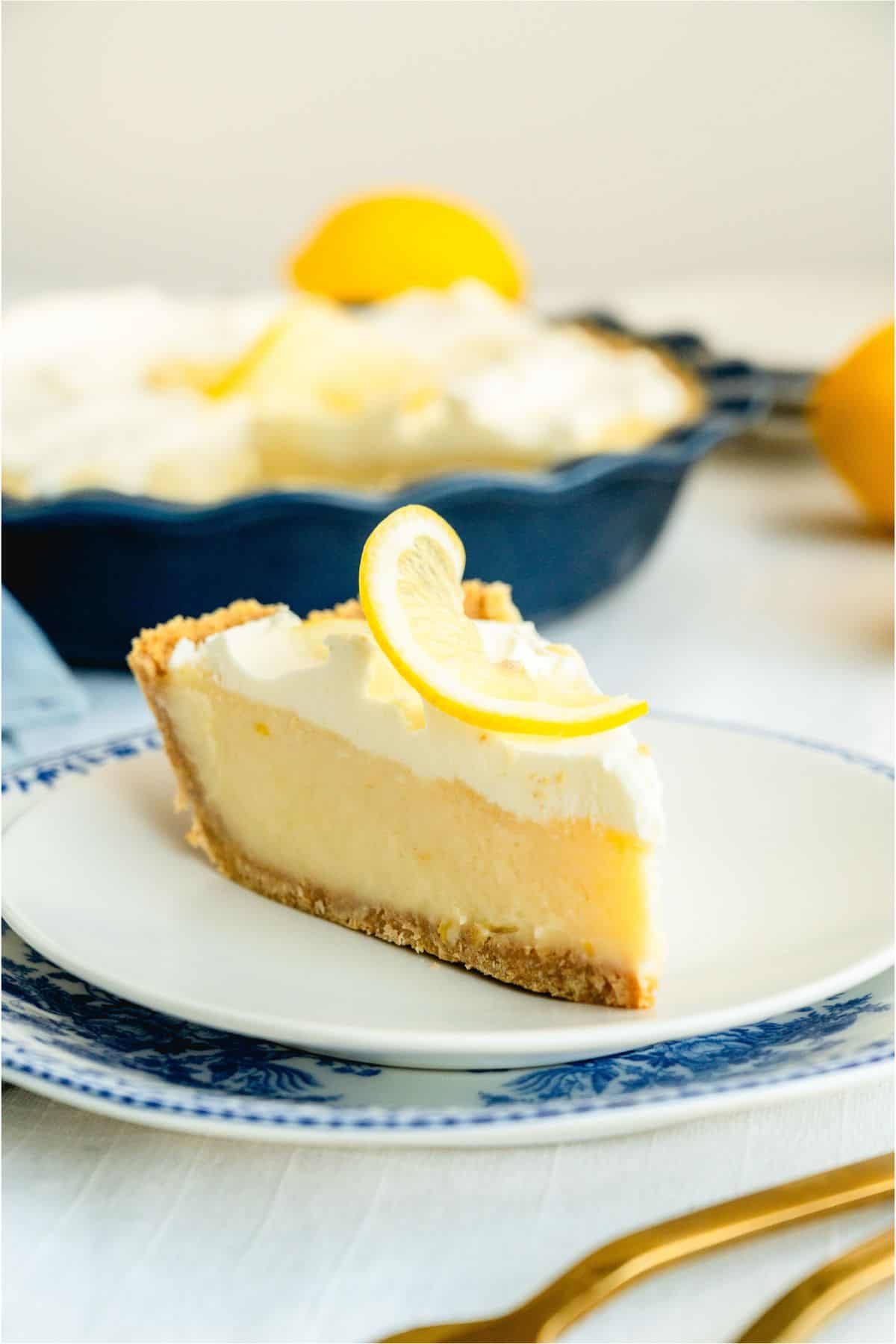 A slice of Creamy Lemon Pie on a plate with the remaining Creamy Lemon Pie in the background