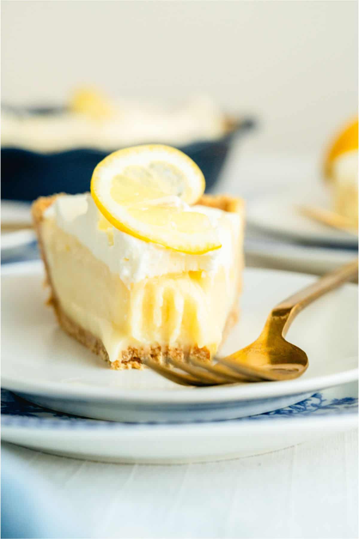 A slice of Creamy Lemon Pie on a plate with a for and a bite missing