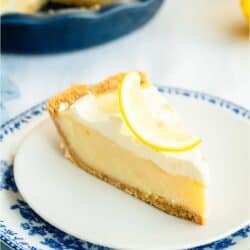 A slice of creamy lemon pie on a plate topped with fresh lemon spiral. With the remaining Creamy Lemon Pie in the background.