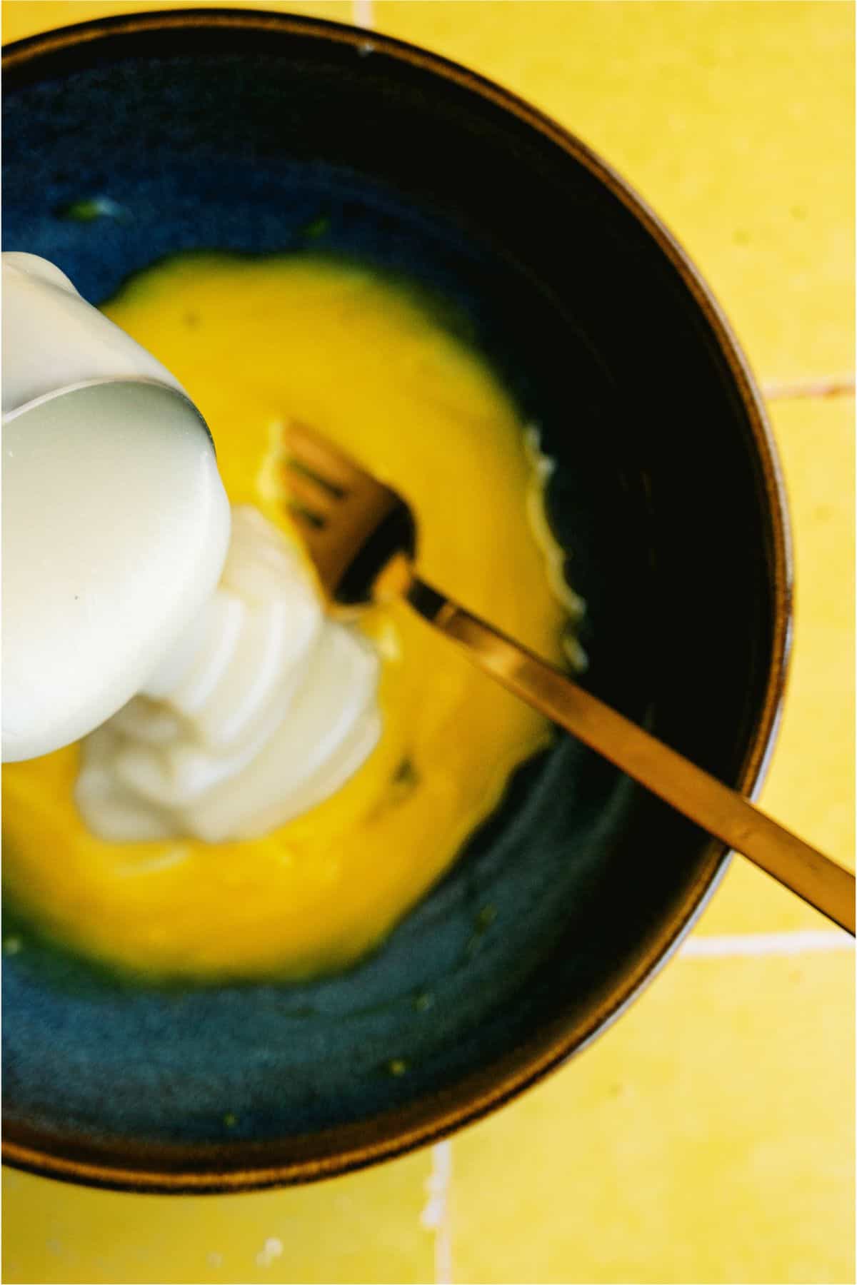 Measuring cup pouring milk into a saucepan with lemon mixture.