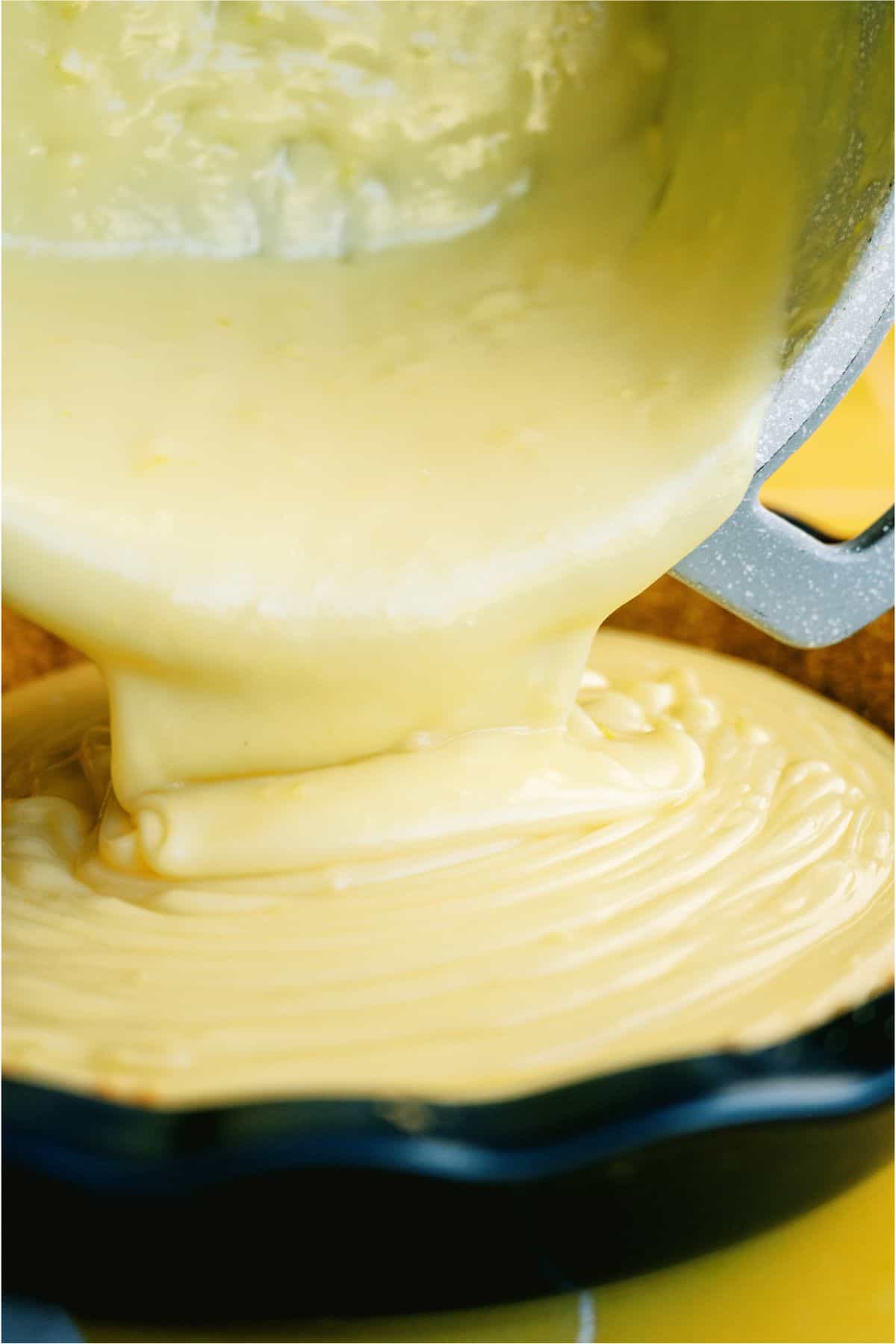 Pouring Lemon pie filling into pie shell from saucepan.