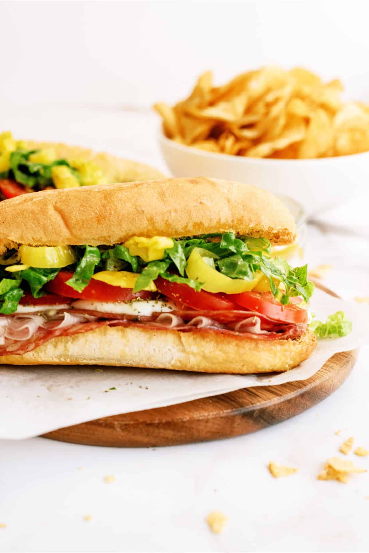 A Hot Italian Trio Sandwich on a cutting board with a bowl of chips in the background