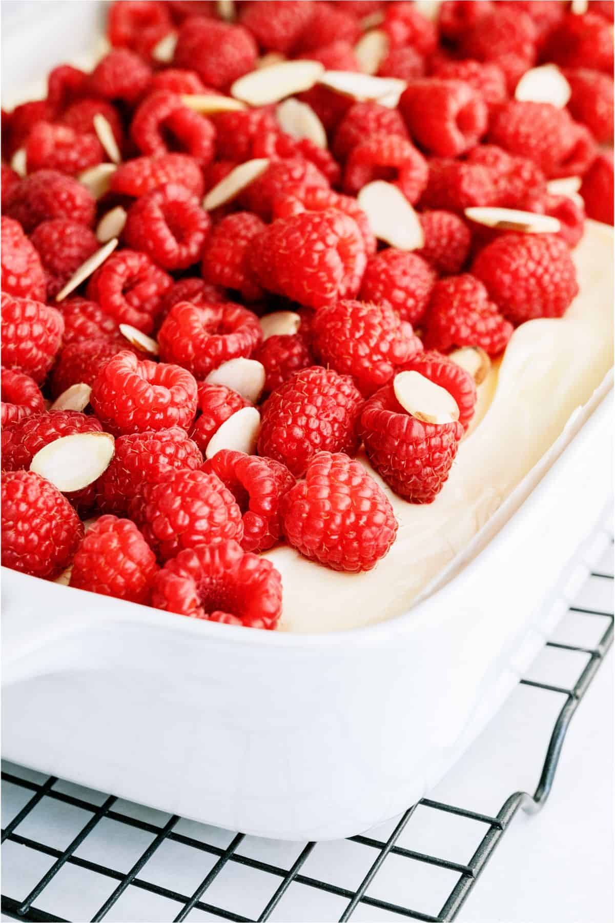 Close up of White Raspberry Poke Cake topped with fresh raspberries and sliced almonds.