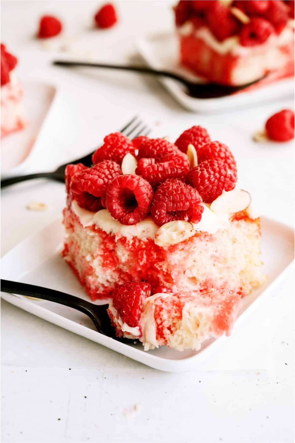 A slice of White Raspberry Poke Cake on a plate with a fork taking a bite out.