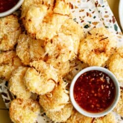 A platter of golden-brown coconut shrimp arranged around two small bowls of red dipping sauce.