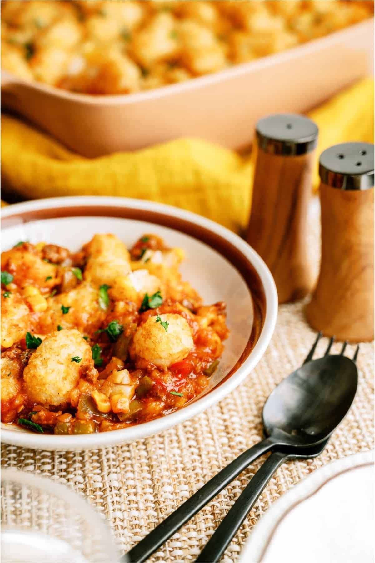 A serving of BBQ Tater Tot Casserole in a bowl with the remaining BBQ Tater Tot Casserole in the background