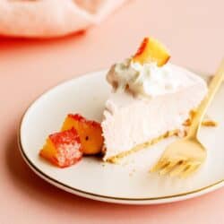 A slice of Creamy Peach Pie on a small plate with a fork topped with whip cream and fresh peaches.