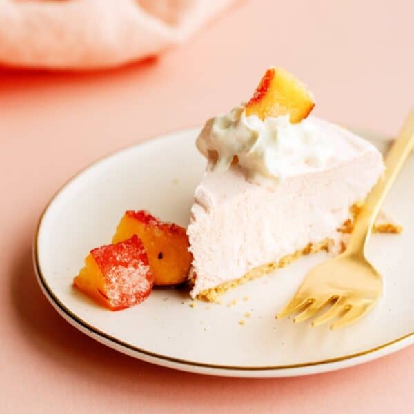 A slice of Creamy Peach Pie on a small plate with a fork topped with whip cream and fresh peaches.