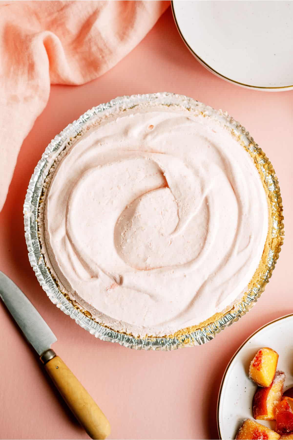 Top view of Creamy Peach Pie on a countertop with a knife and chopped peaches on a plate to the side.