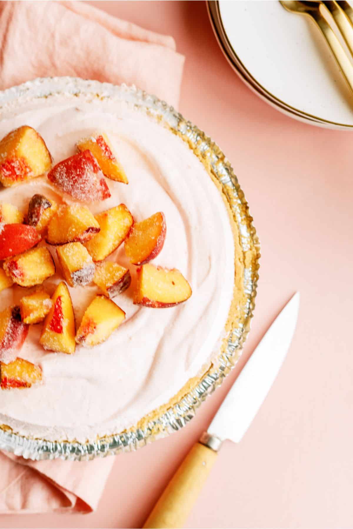 Creamy Peach Pie topped with fresh chopped peaches and a pairing knife next to the pie.
