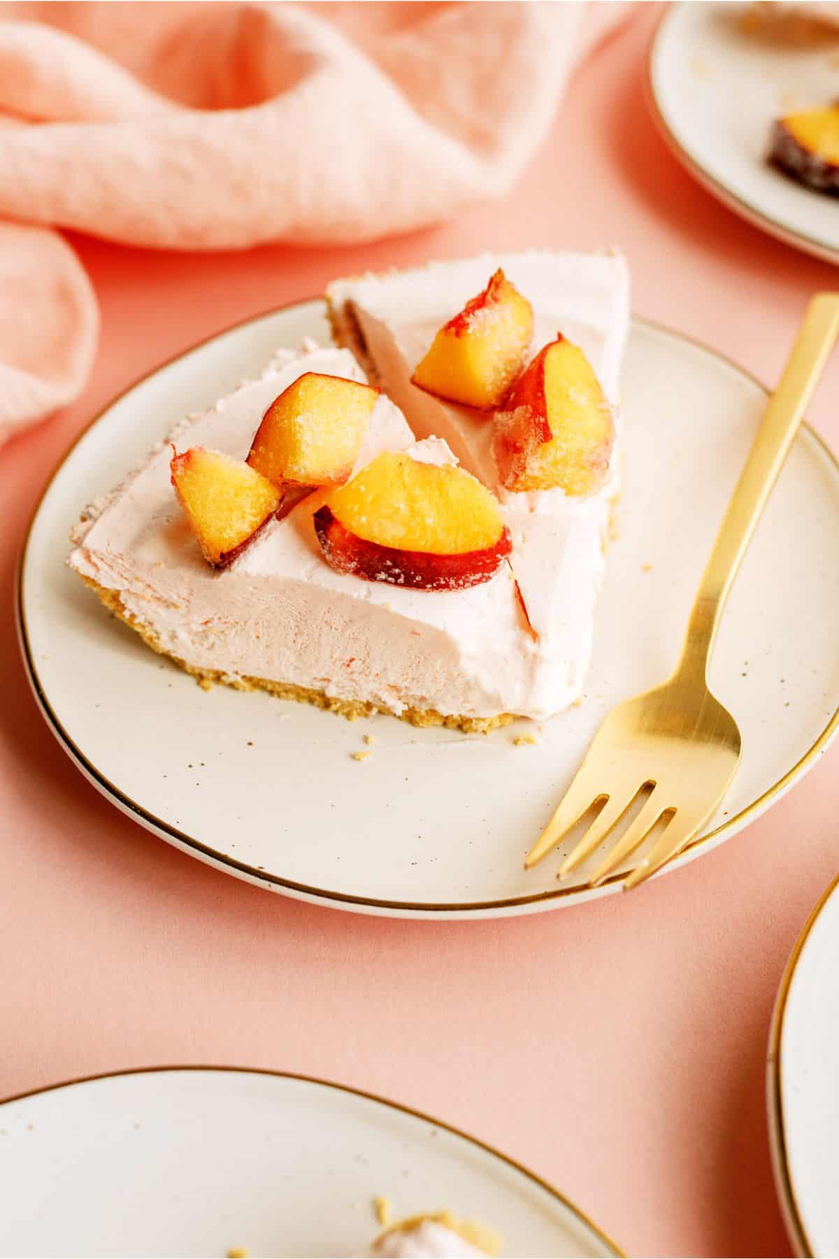 Two slices of Creamy Peach Pie on a plate with a fork, topped with fresh peaches.
