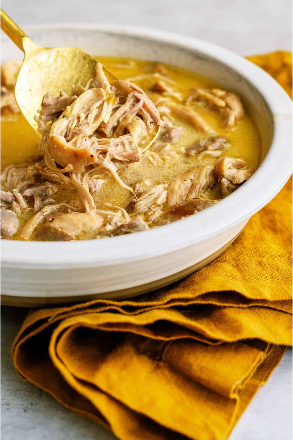 Shredded chicken in a bowl with sauce and a spoon lifting out shredded chicken