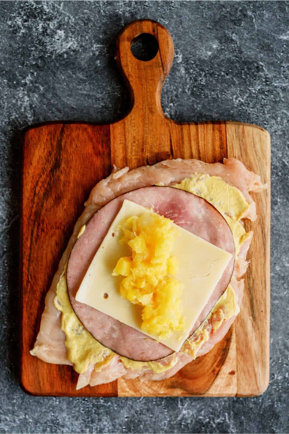 Flattened chicken breast with sauce, ham, swiss and pineapple layered on top