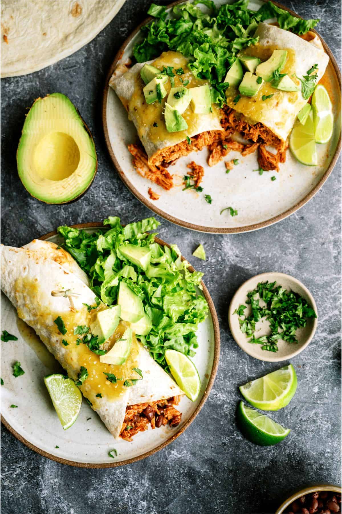 2 plates with Slow Cooker Mexican Shredded Pork Burritos and toppings