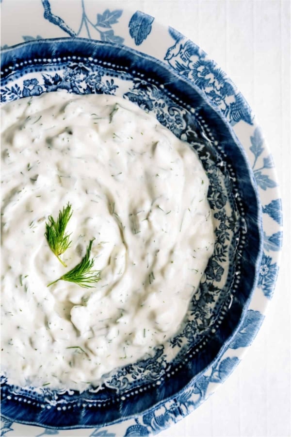 A bowl of creamy white dip with herbs, garnished with fresh dill, served in a blue and white patterned dish.
